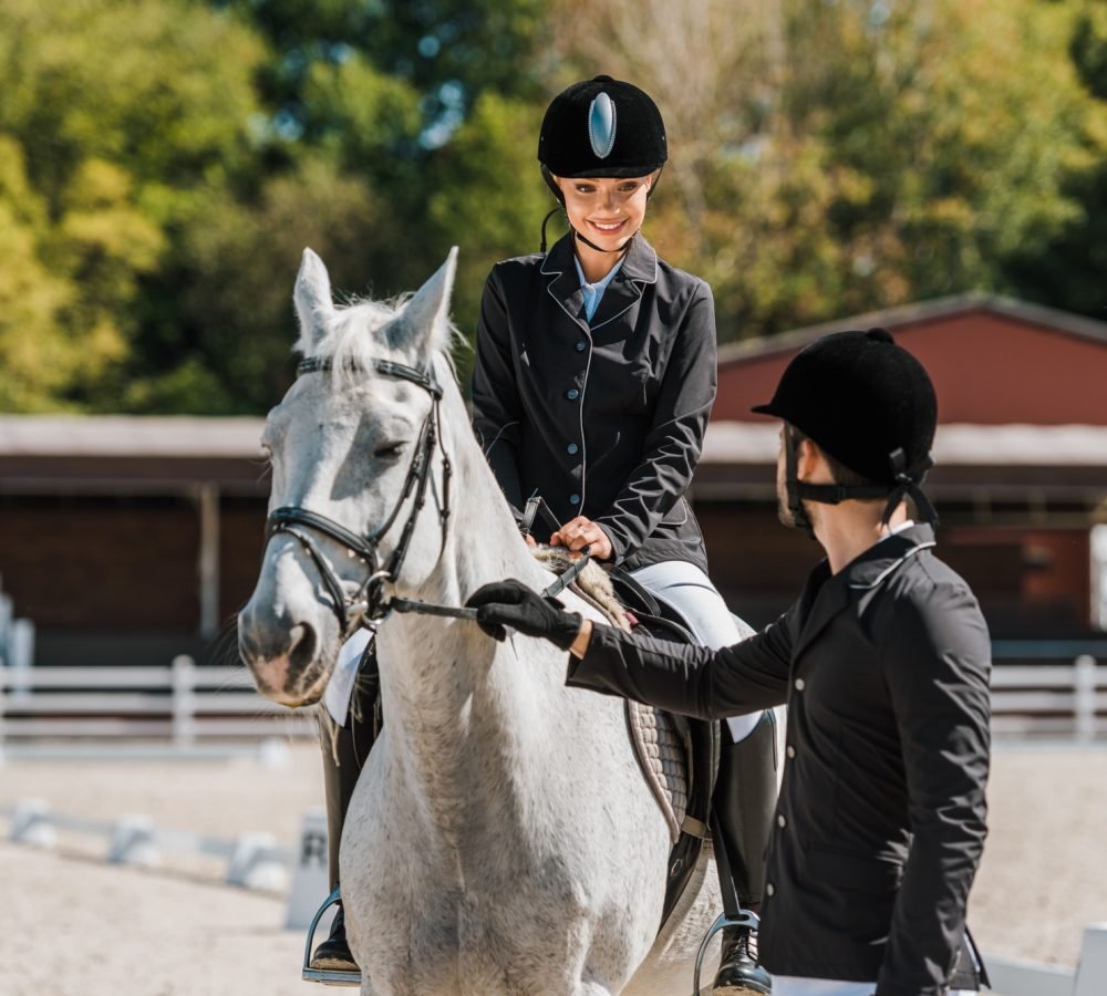 male-equestrians-holding-horse-halter-female-jockey-sitting-on-horse-at-horse-club.jpg